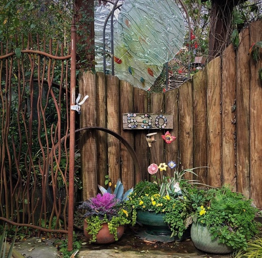 Felderyard entry with artisan gate, glass sculpture., and ceramic flowers